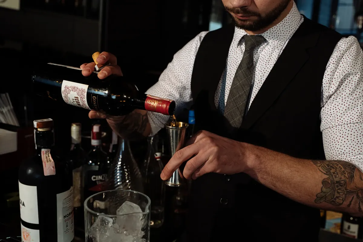 Bartender skillfully measures and pours red wine in a bar setting.