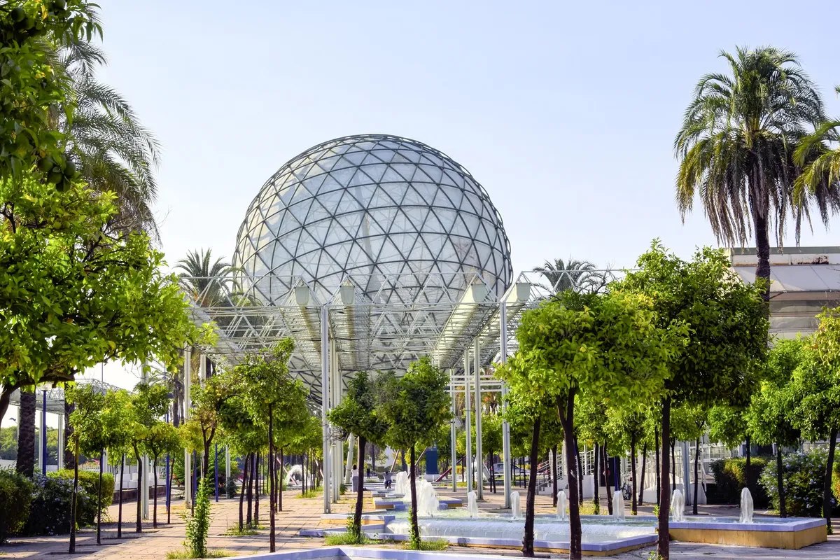 Geodesic dome amidst lush greenery and water fountains at Seville Expo park.