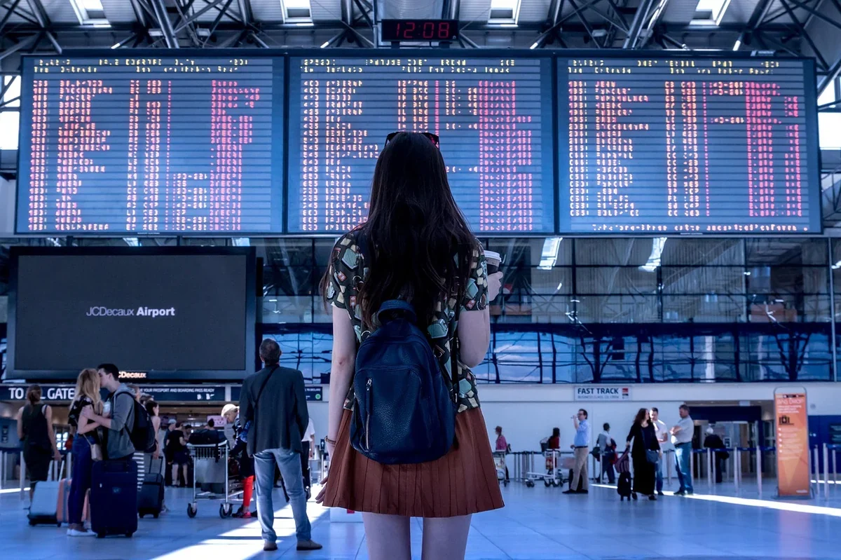 Una persona mirando un gran tablero digital de salidas en un aeropuerto